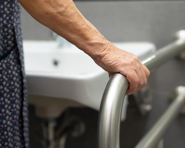 Mano anziana su corrimano in bagno per sicurezza.