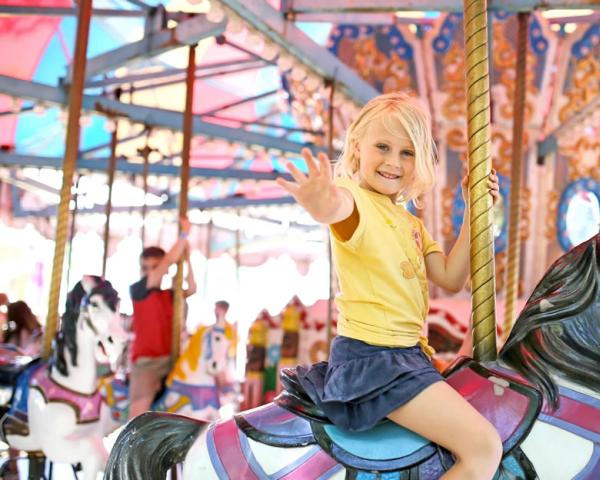 Bambina su giostra sorridente, indossa maglietta gialla.