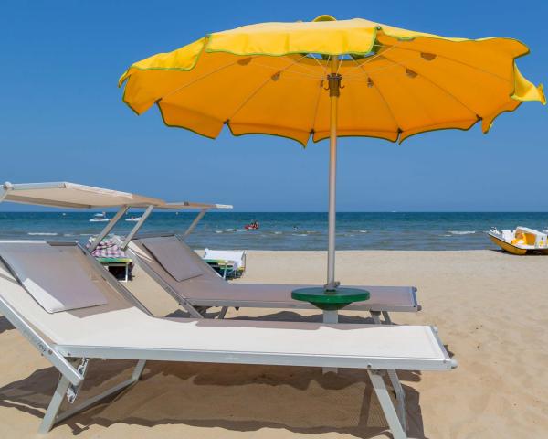 Spiaggia con lettini, ombrellone giallo e pedalò sullo sfondo.